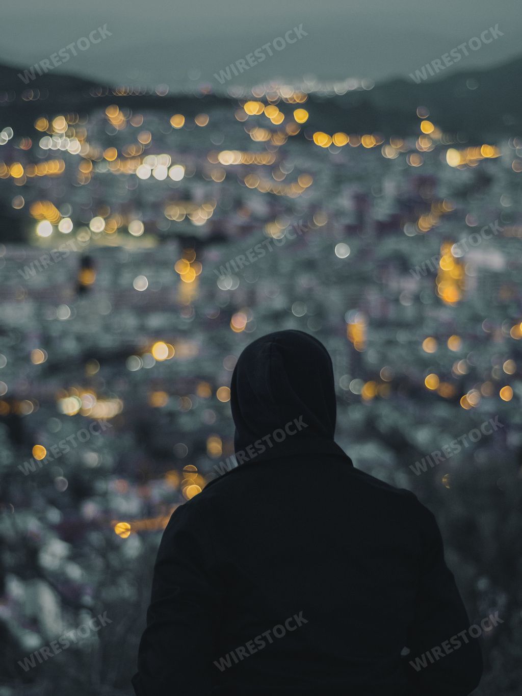 A silhouette of a man overlooking the bright city with bokeh lights in the evening