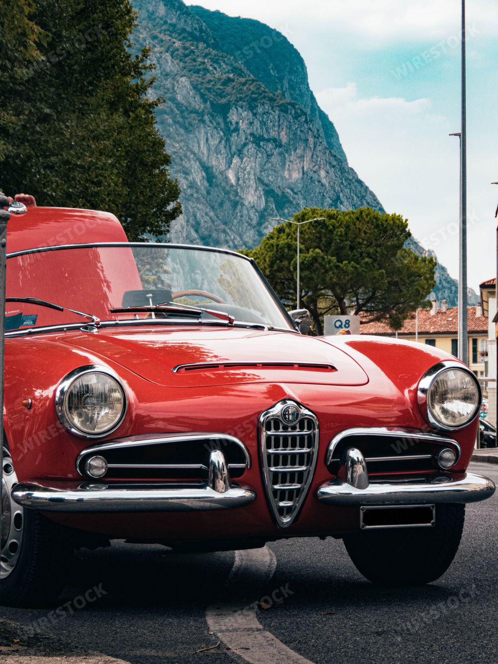 A vertical shot of a red Alfa Romeo Giulietta on a street in Lecco, Italy