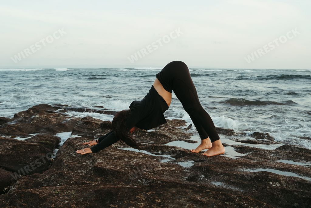 Young woman doing yoga Downward facing Dog pose on the beach in Bali. Adho mukha svanasana pose