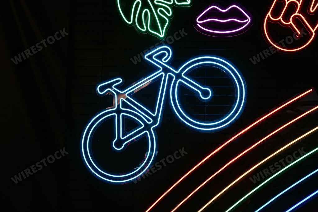 An illuminated neon sign with a bicycle silhouette displayed on a black wall at a cafe at night