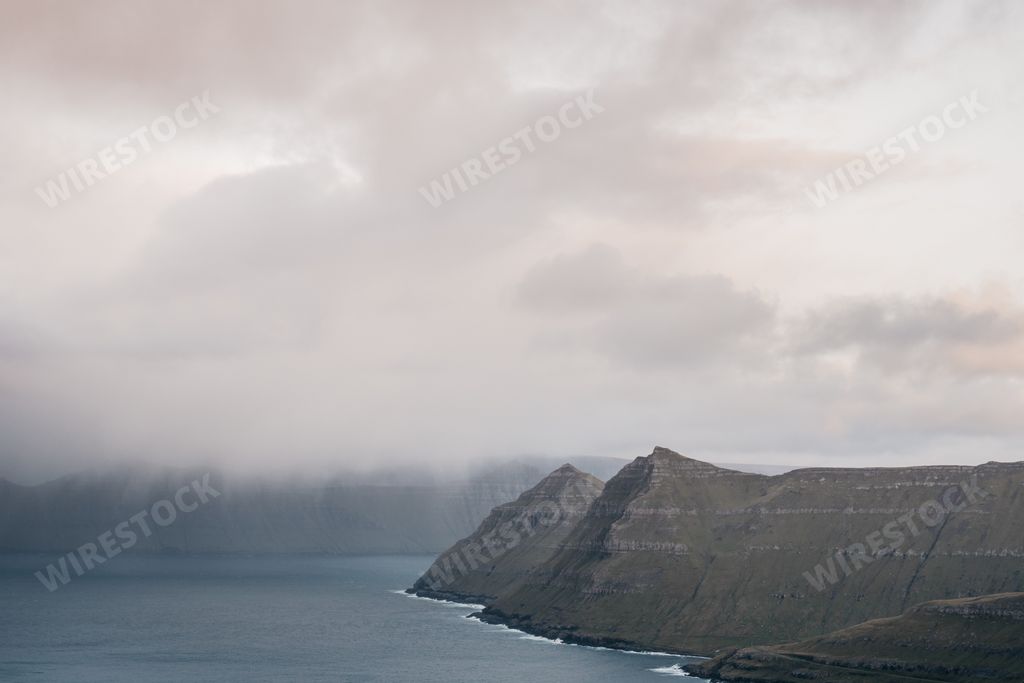 Faroe cliffs in mist. Morning Scandinavian landscape with mountains and fog over the fjord. Nordic landscape