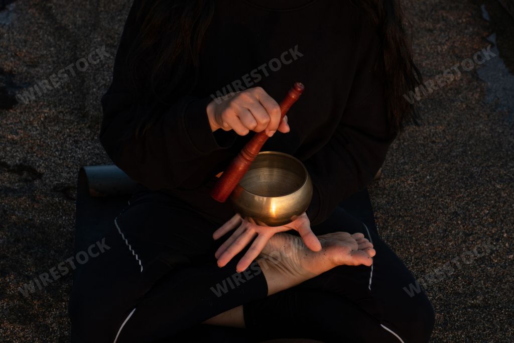 Woman playing Tibetan singing bowl during a meditation and relaxation session in Bali beach. Sound healing, stress relief