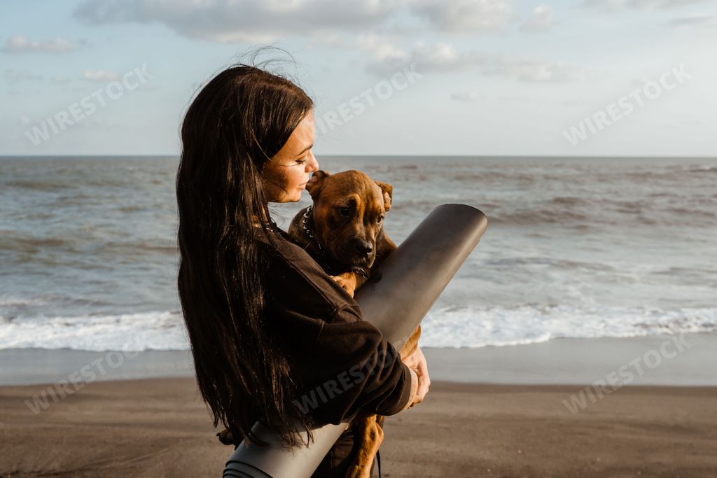 Beautiful caucasian woman carries American bully puppy. Ocean background. Healthy and sporty lifestyle