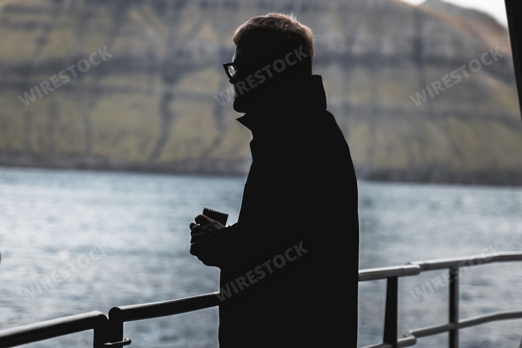 Silhouette of a man standing on sailing boat, Scandinavian nordic background, cold Atlantic ocean and mountains