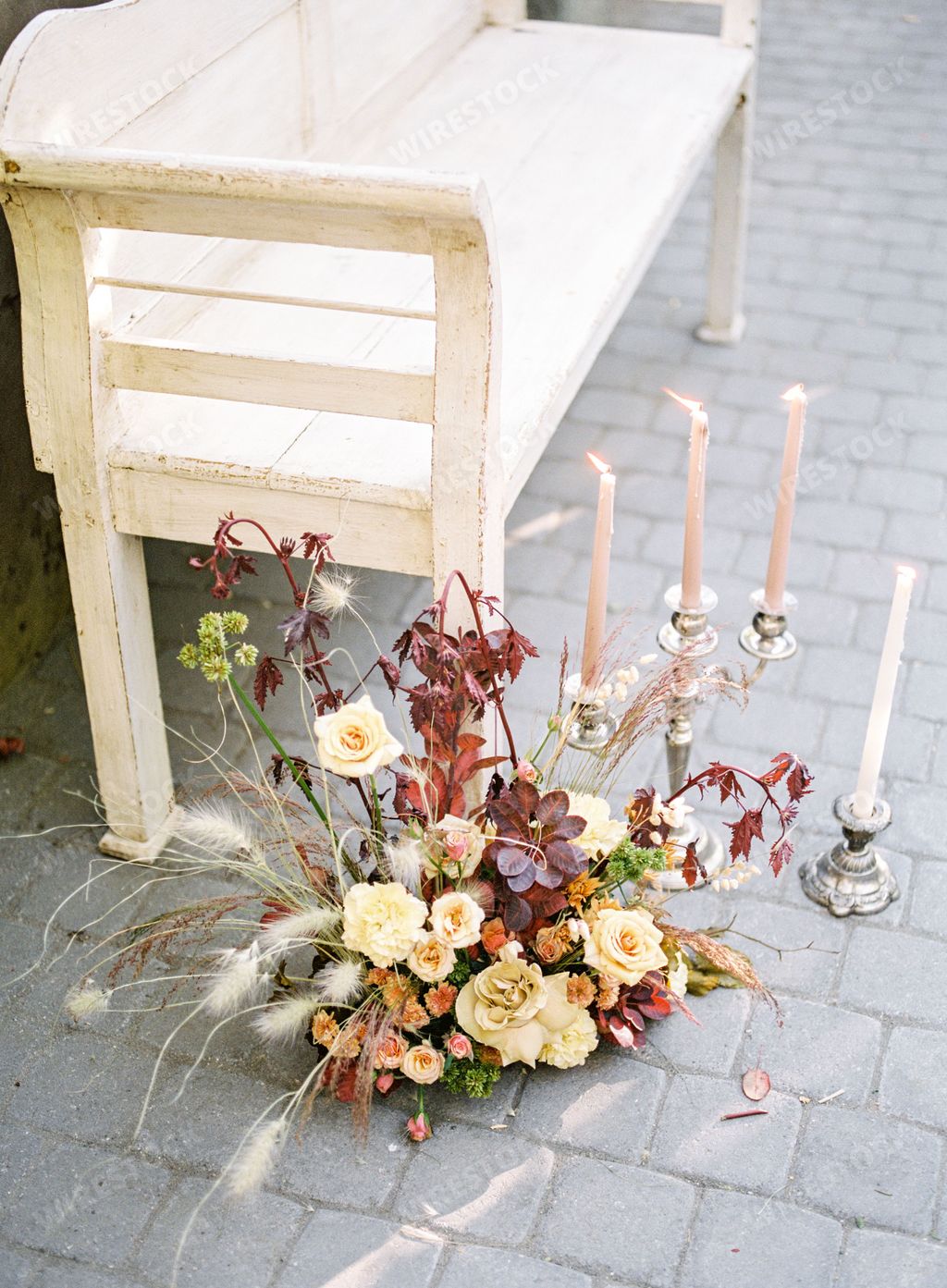 Orange garden roses bouquet and chandelier with candles next to an empty wooden long seat