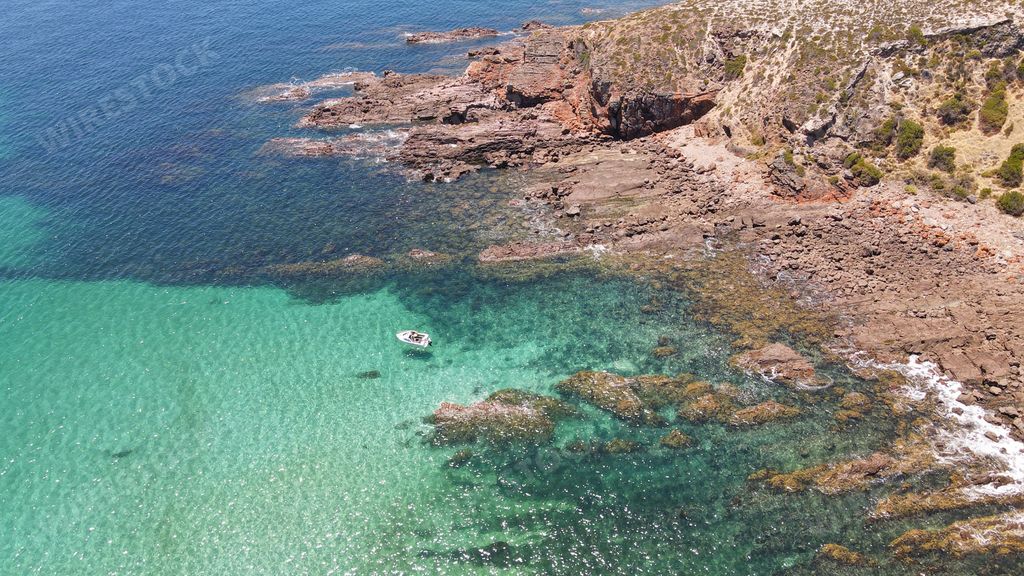An aerial view of rocky beach surrounded by emerald water