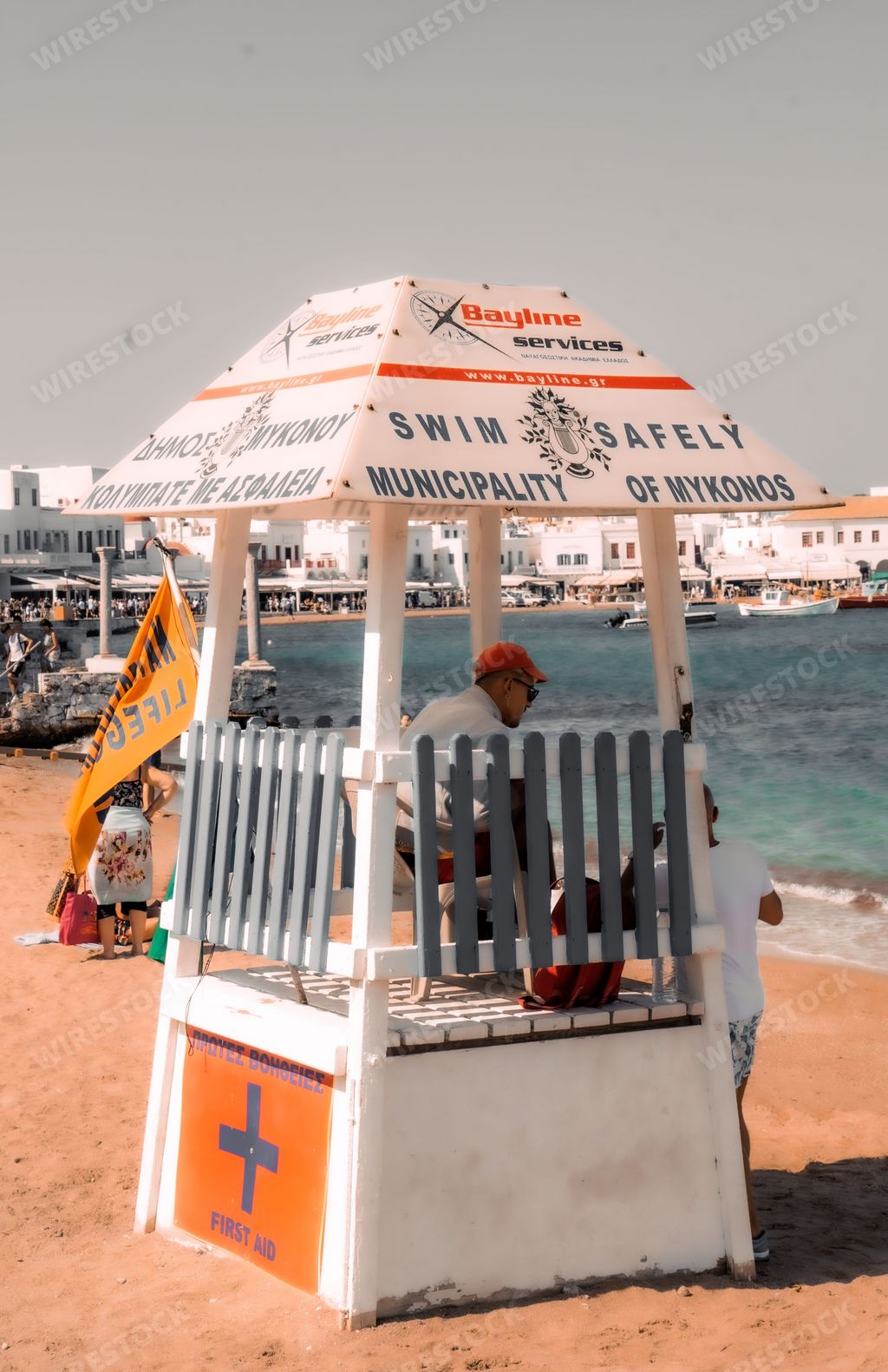 An idyllic beach scene featuring a lifeguard station in the foreground, with people relaxing and enjoying the day in the background