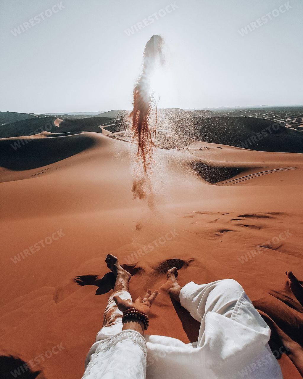 A superb shot of a male sitting on Sahara desert and scattering sands towards the bright sun