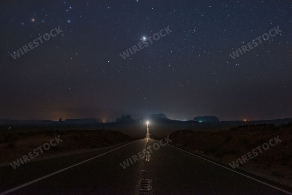 A horizontal shot of an empty road with a light at the end in the Monument Valley, USA under the breathtaking starry night sky
