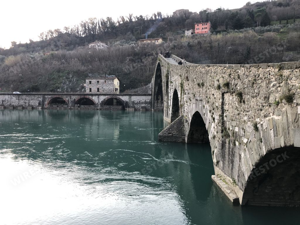 The Ponte Della Maddalena bridge surrounded by hills and greenery in Borgo a Mozzano in Italy