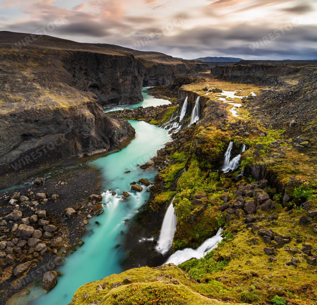 A high angle shot of waterfalls in Highlands region of Iceland with a cloudy gray sky in the background