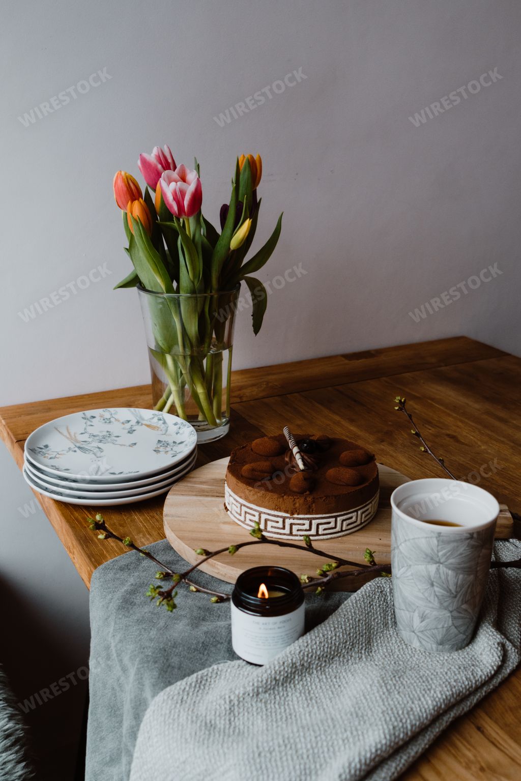 A vertical shot of tulips in a vase, a cup of espresso and a delicious chocolate cake on a table