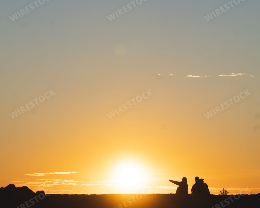 A horizontal shot of two people in silhouette sitting on the ground during sunset. Perfect for a travel blog