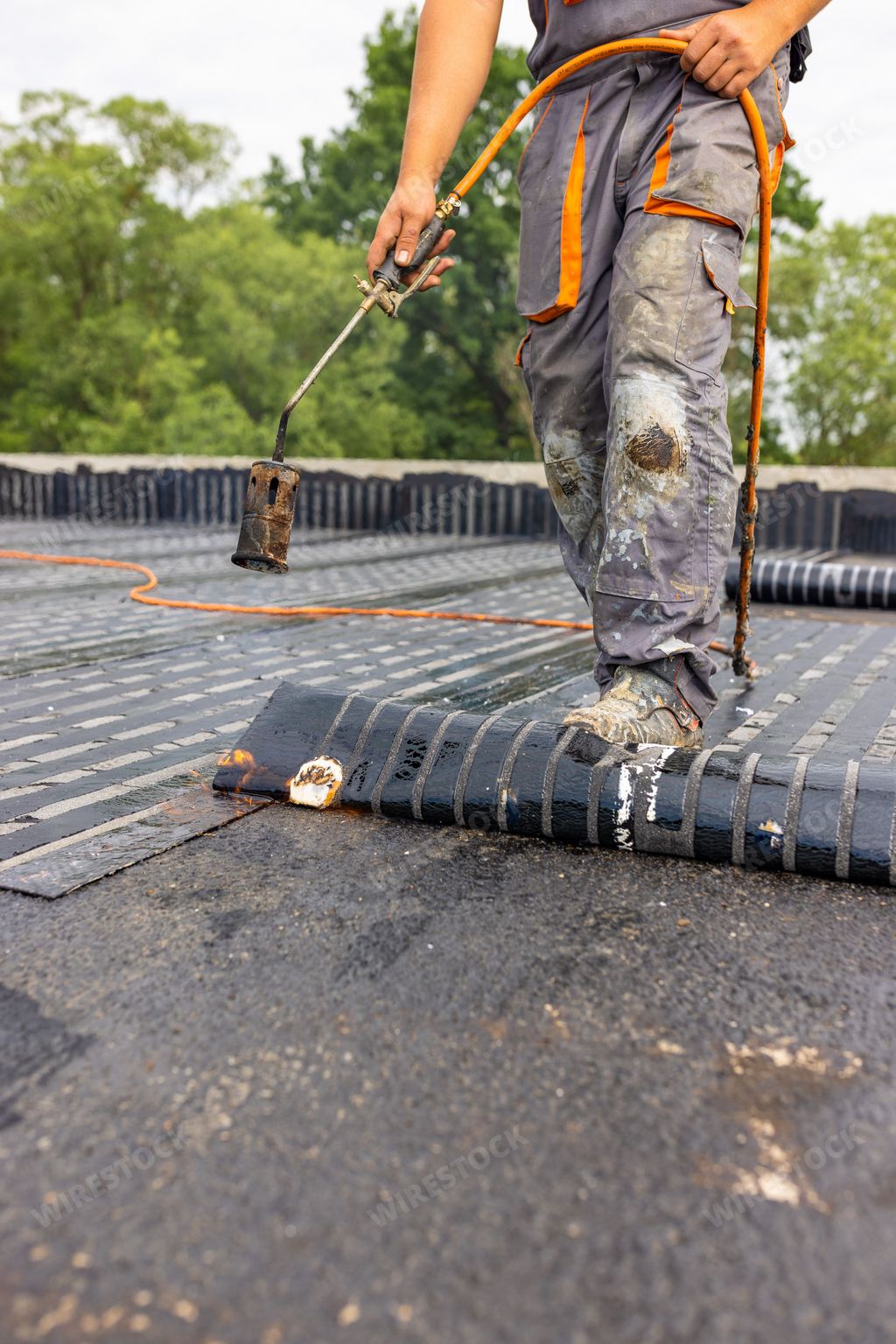 A worker placing a vapor barrier on the roof using a propane gas torch for welding bitumen sheets