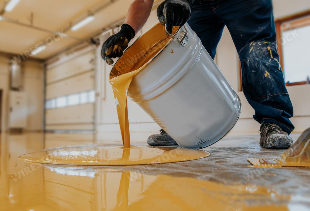 A closeup shot of a construction worker pouring out epoxy resin from a bucket onto a floor