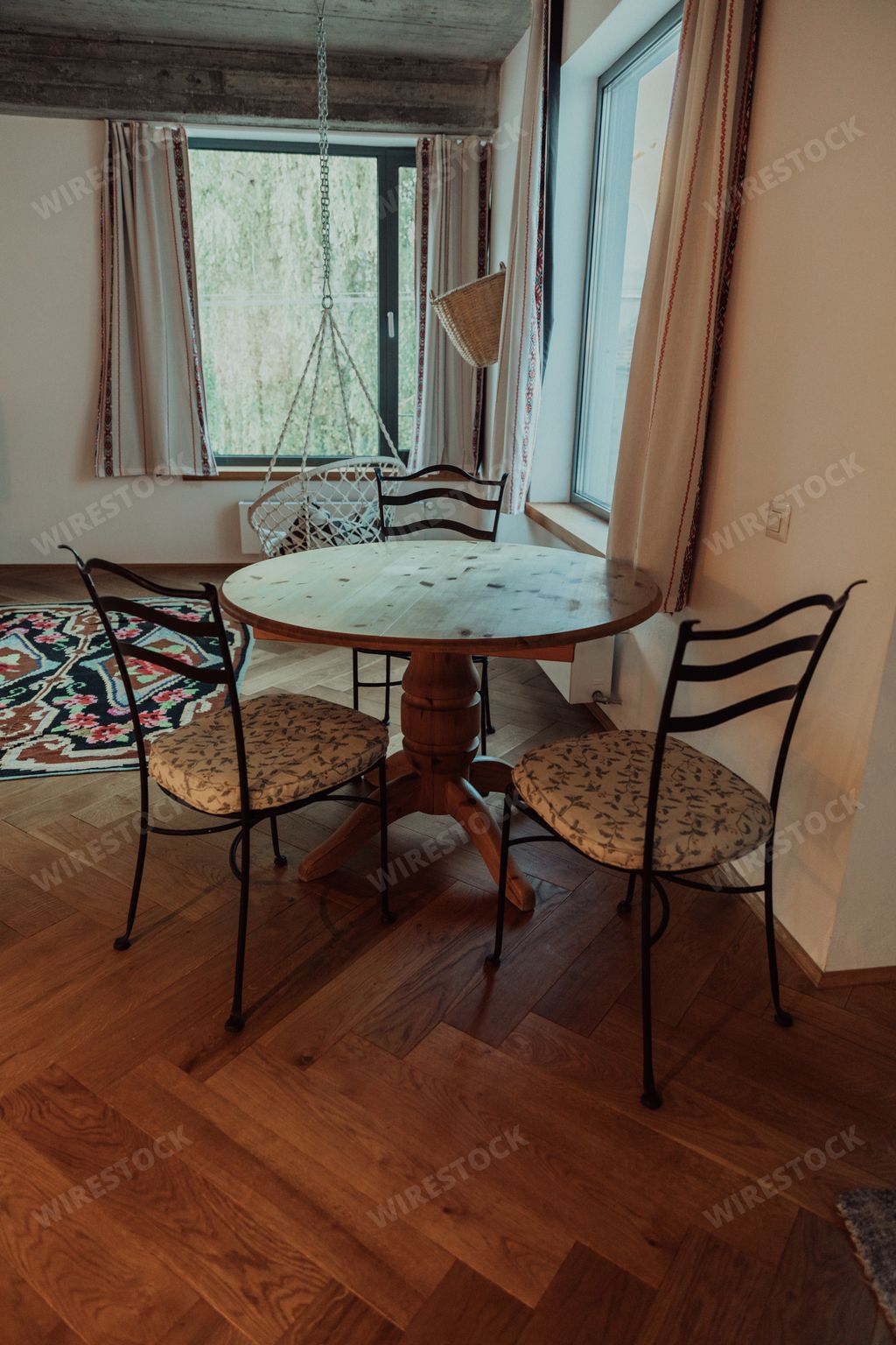 a loft-style room with table and chairs, colorful carpet on the wooden floor and a hanging chair