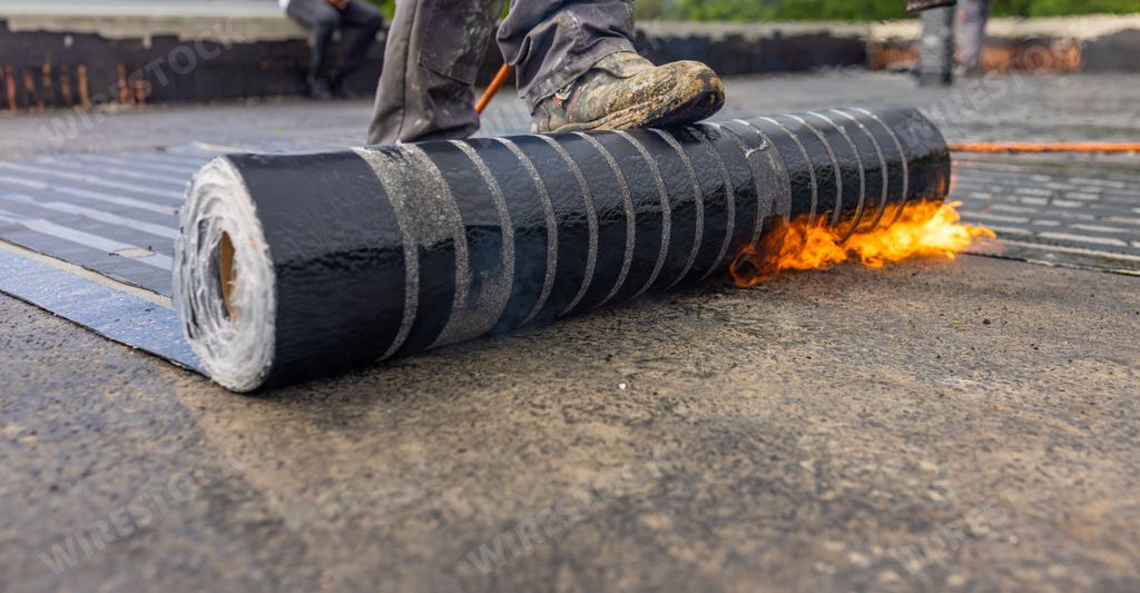 A worker placing a vapor barrier on the roof using a propane gas torch for welding bitumen sheets