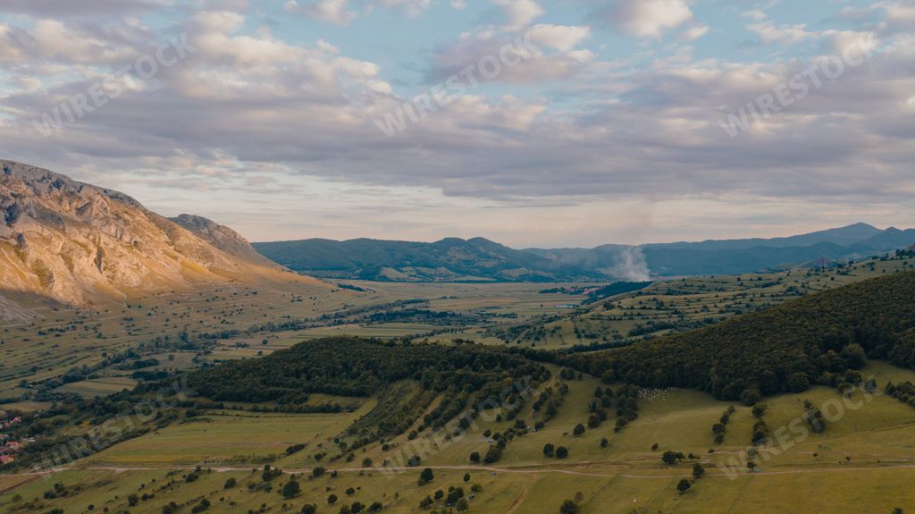A view of a scenic valley with green hills and mountains in the background; Rimetea village in Romania