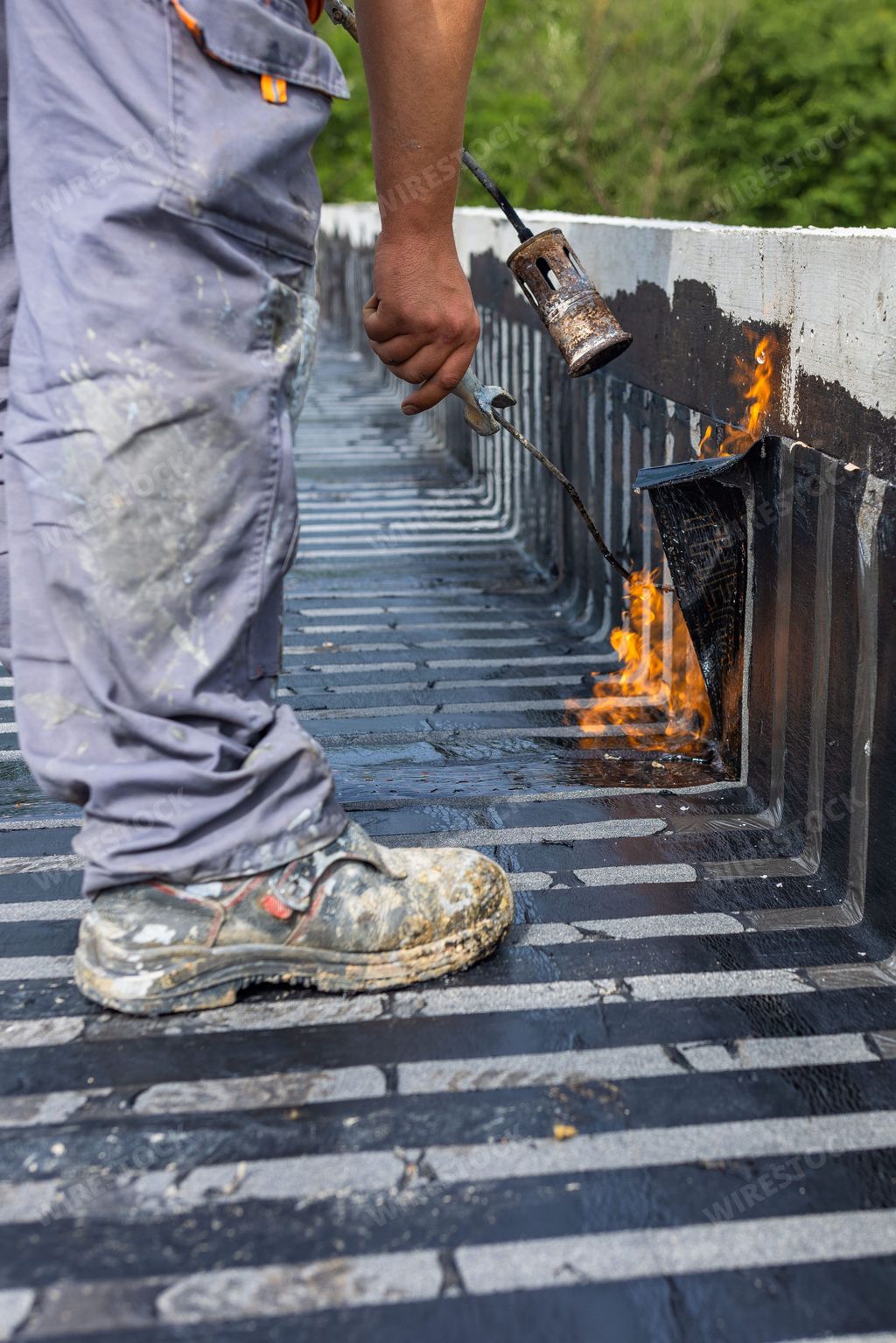 A worker placing a vapor barrier on the roof using a propane gas torch for welding bitumen sheets