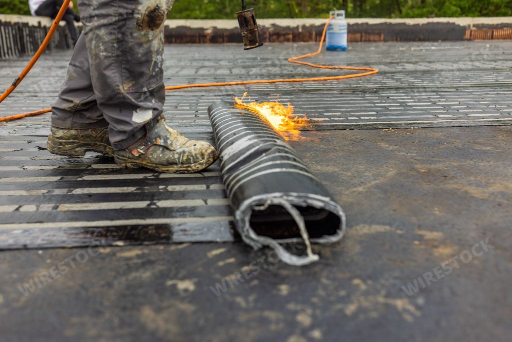 Worker placing a vapor barrier on the roof using a propane gas torch ...