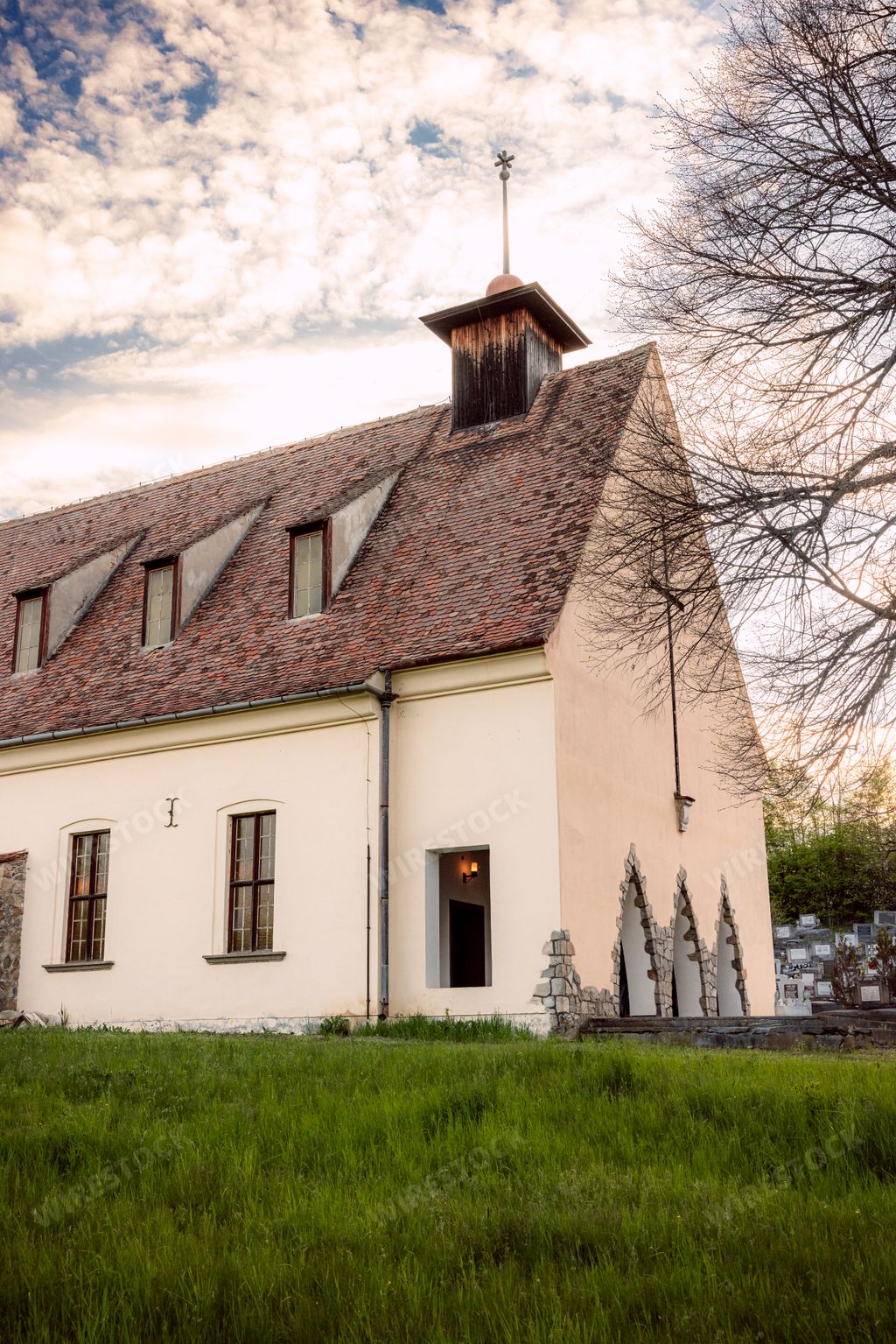 A rustic white barn with a brown roof and a weather vane perched atop sits in an idyllic rural setting