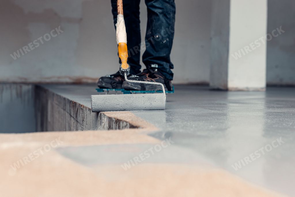 A  close up shot of a construction worker applying grey epoxy resin in an industrial hall