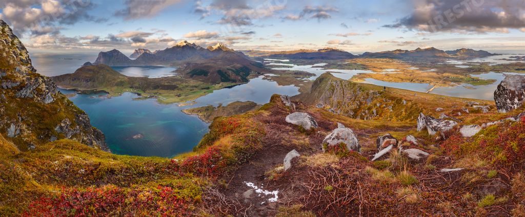 A panoramic shot of grassy hills and mountains near water under a blue cloudy sky in Norway