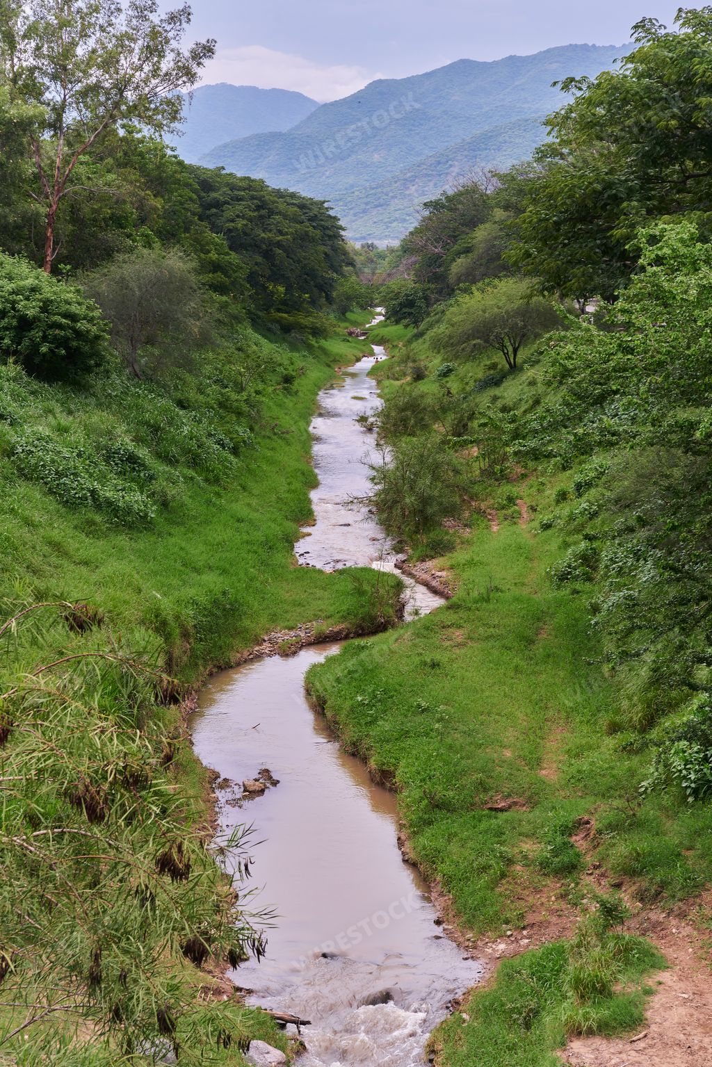 A small river crossing in the middle of some mountains with a very greenish landscape