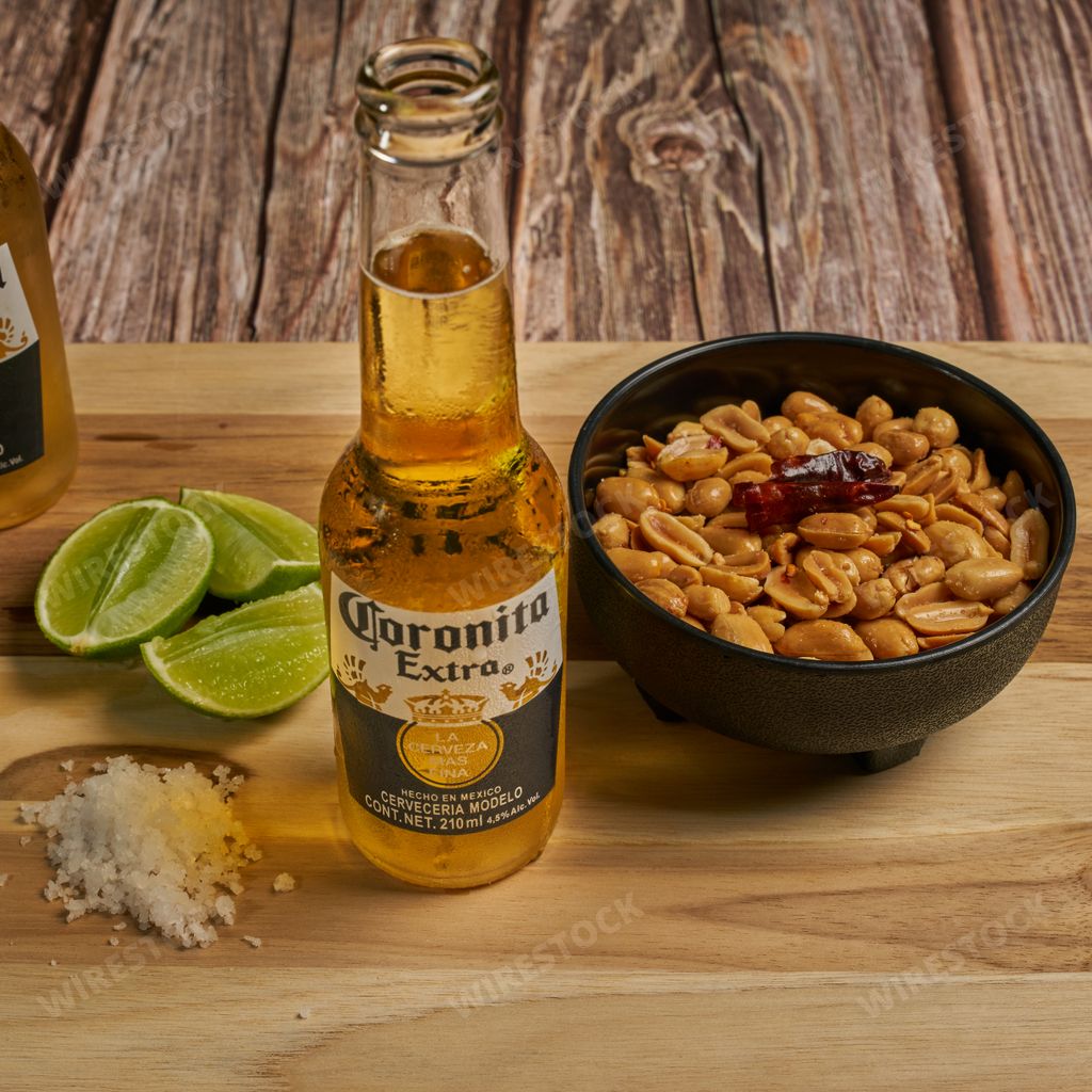 A closeup shot of cold Corona beer with peanuts in bowl, lime pieces and salt on the wooden surface
