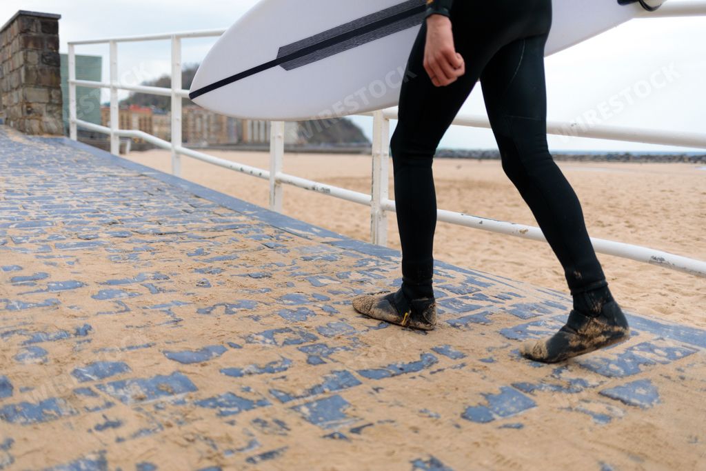 A surfer in a wetsuit walking along a sandy beach while holding a surfing board