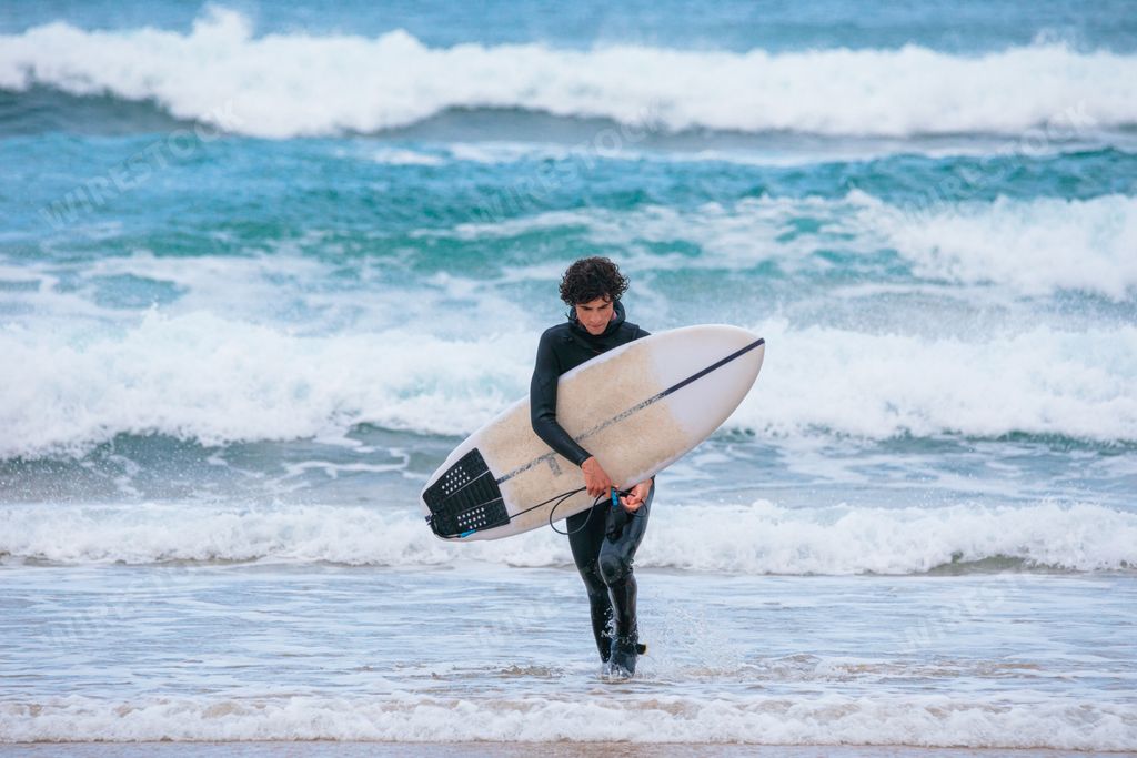 A Caucasian male coming back from surfing in the ocean