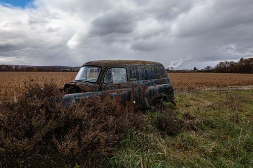 Old rusty car abandoned in the green and brown field under cloudy sky ...