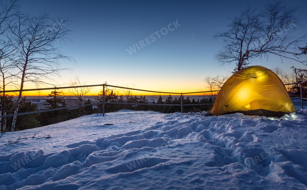 A yellow tent in front of a forest next to a wooden fence at sunset on a cold winter day