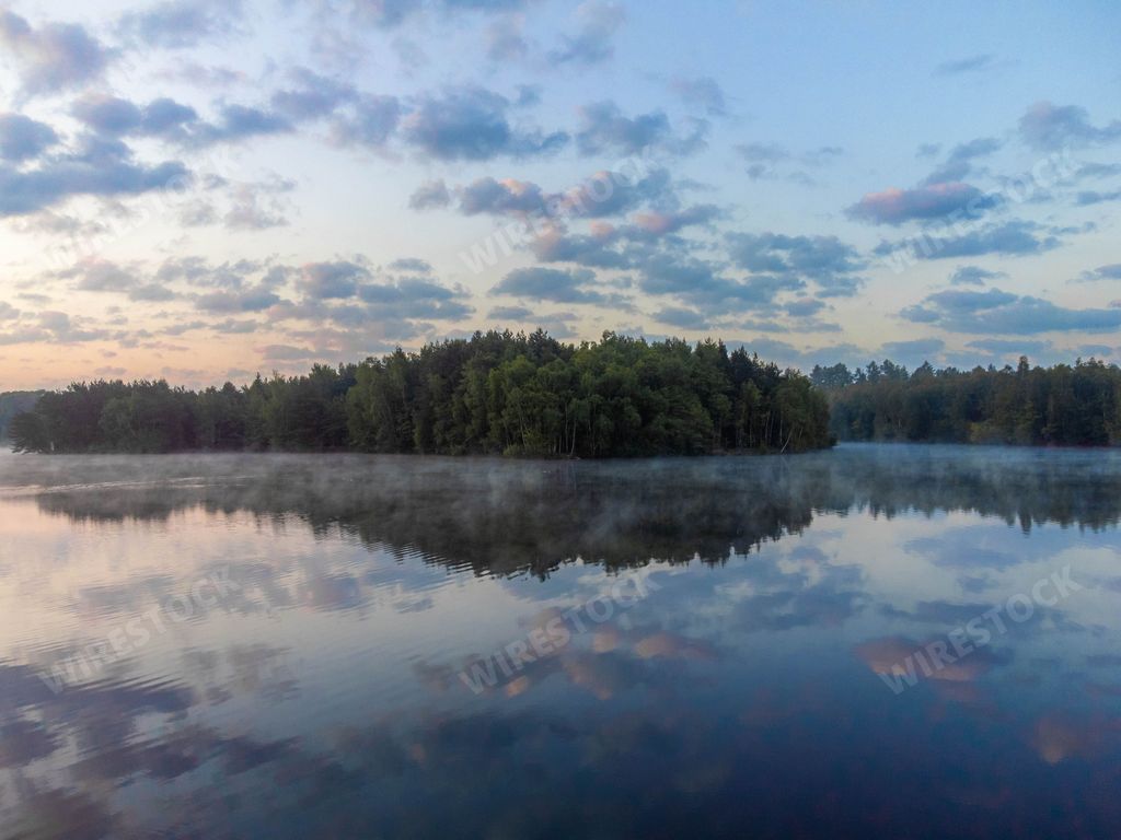 A beautiful shot of a calm lake reflecting trees and sky full of clouds
