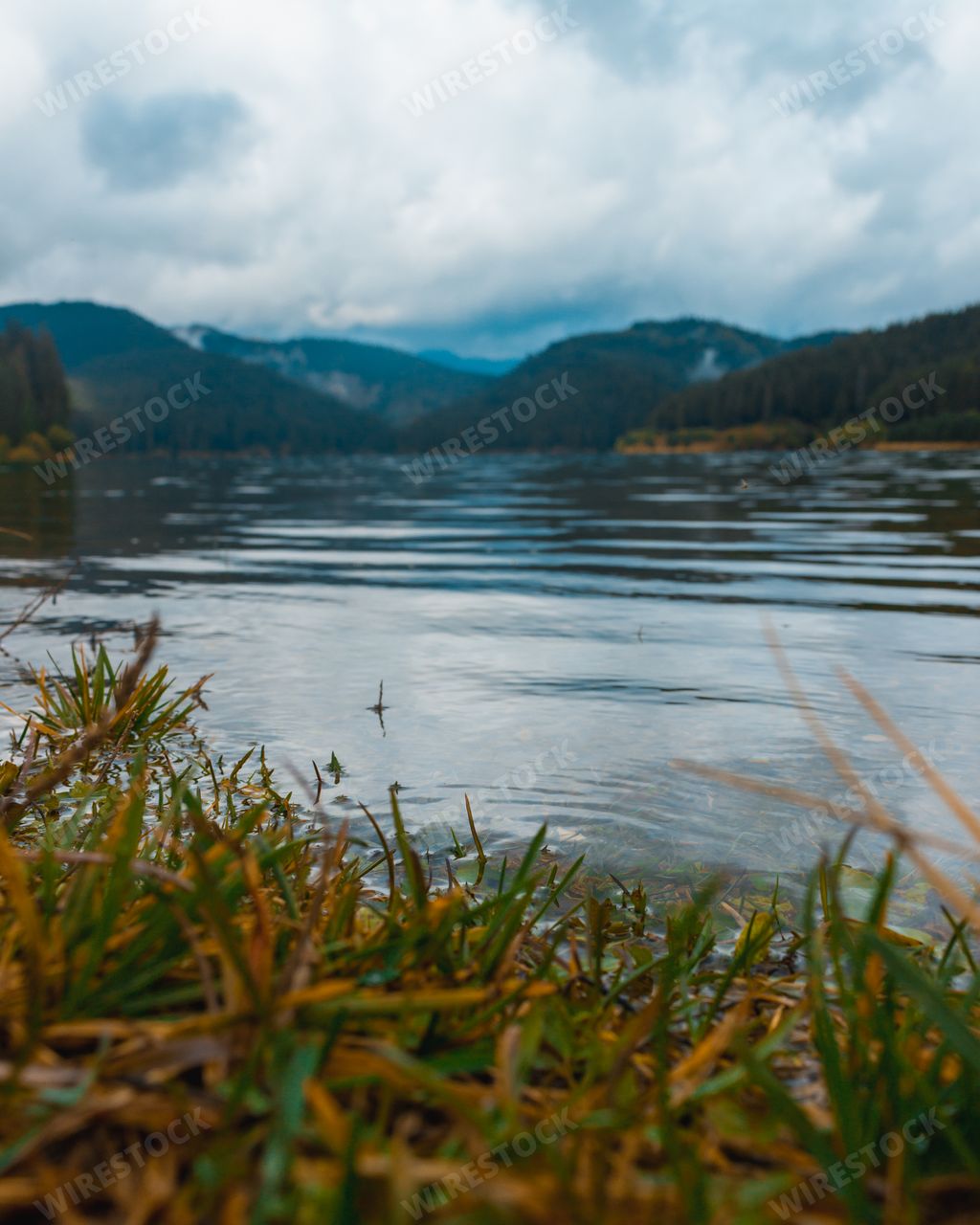 A beautiful scenery of a lake surrounded by rocky mountains under a cloudy sky in Romania