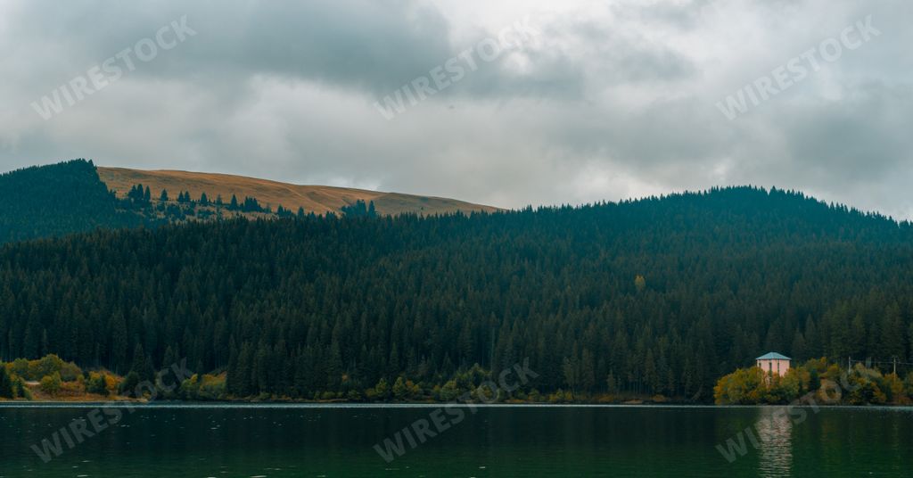 A beautiful scenery of a lake surrounded by rocky mountains under a cloudy sky in Romania