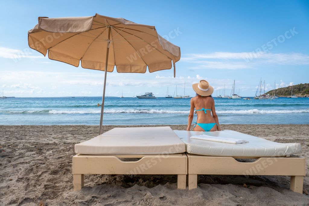 An attractive woman in a bikini looking at the sea sitting on a bed on the beach, Salines, Ibiza, Spain