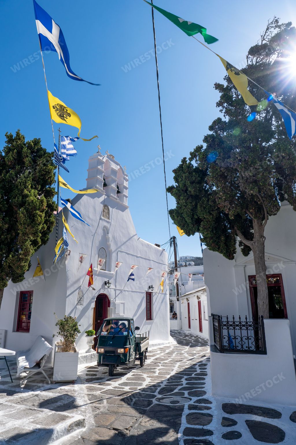 The Agia Kyriaki Church in Mykonos, Greece, illuminated by the sun's rays and surrounded by pink blooms