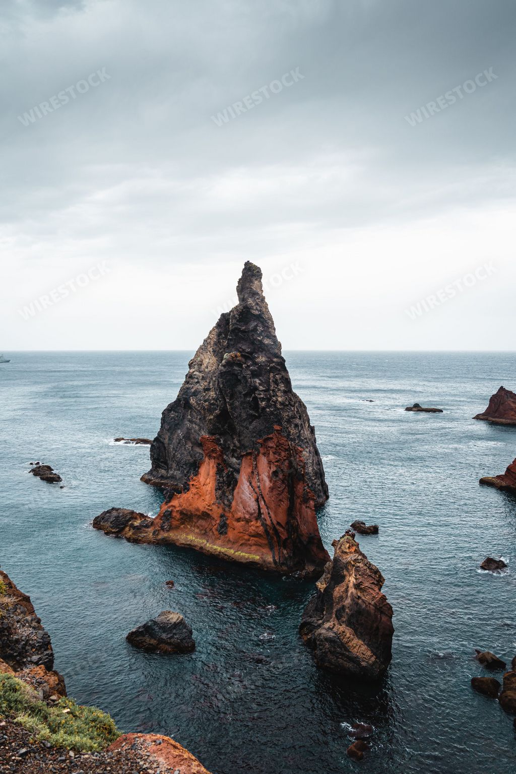 A vertical shot of a rock on a sea with a cloudy sky background in Portugal