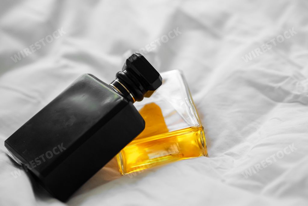 Two luxury perfume bottles on a white bedsheet on a blurred background