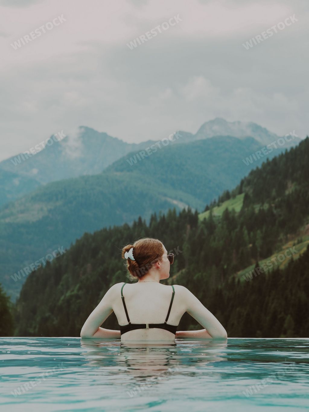 A vertical aesthetic view of a beautiful female in the swimming pool and hills in the background