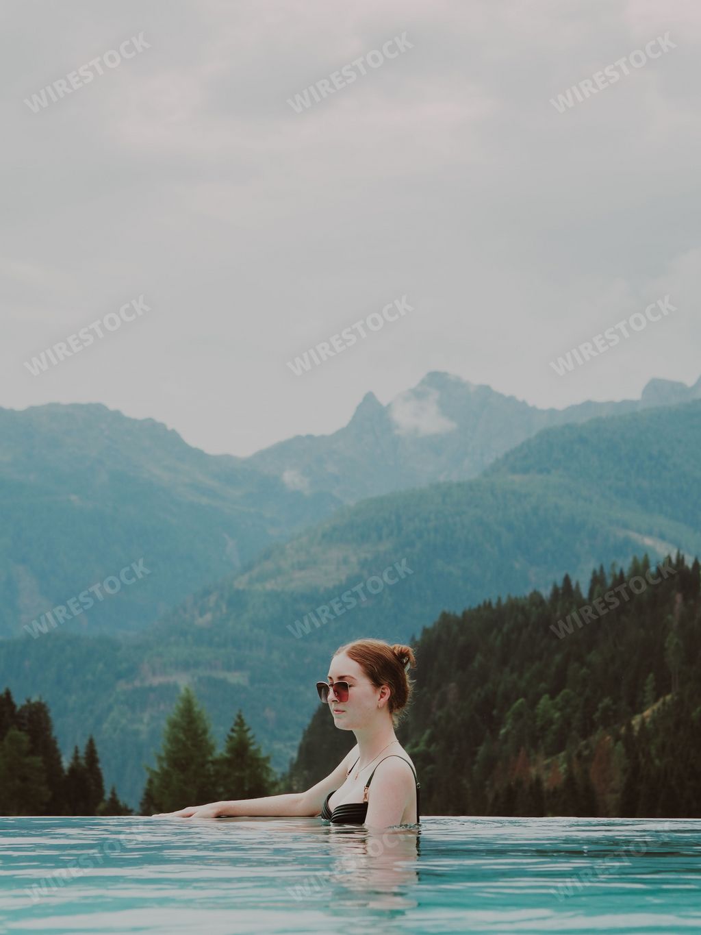 A vertical aesthetic view of a beautiful female in the swimming pool and hills in the background