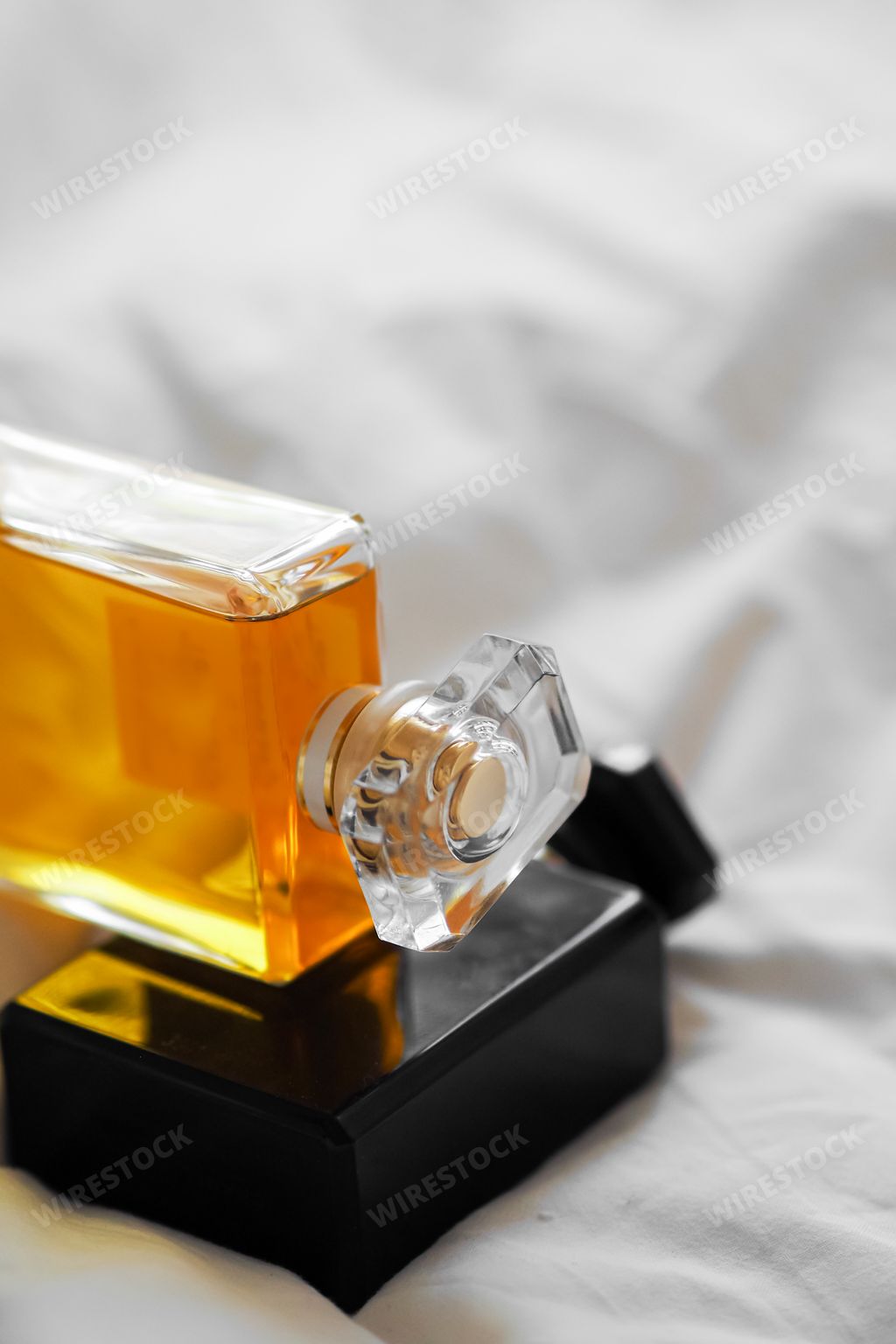 A vertical shot of two perfume bottles on a white bedsheet on a blurred background
