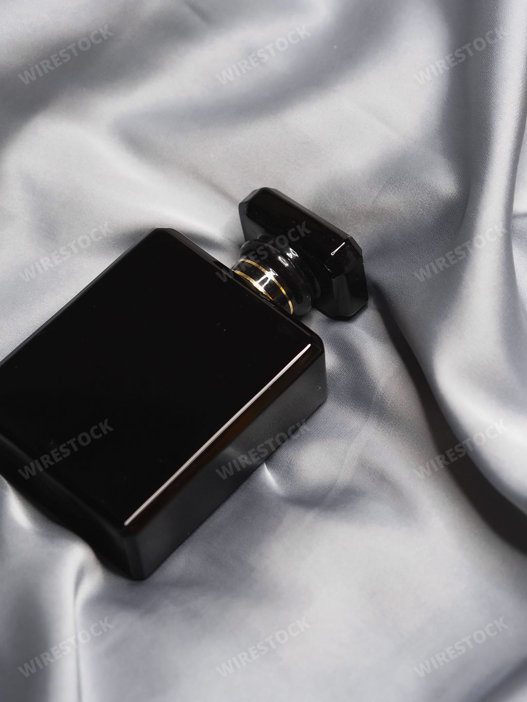 A vertical closeup high-angle shot of a black perfume bottle on a grey silk cloth