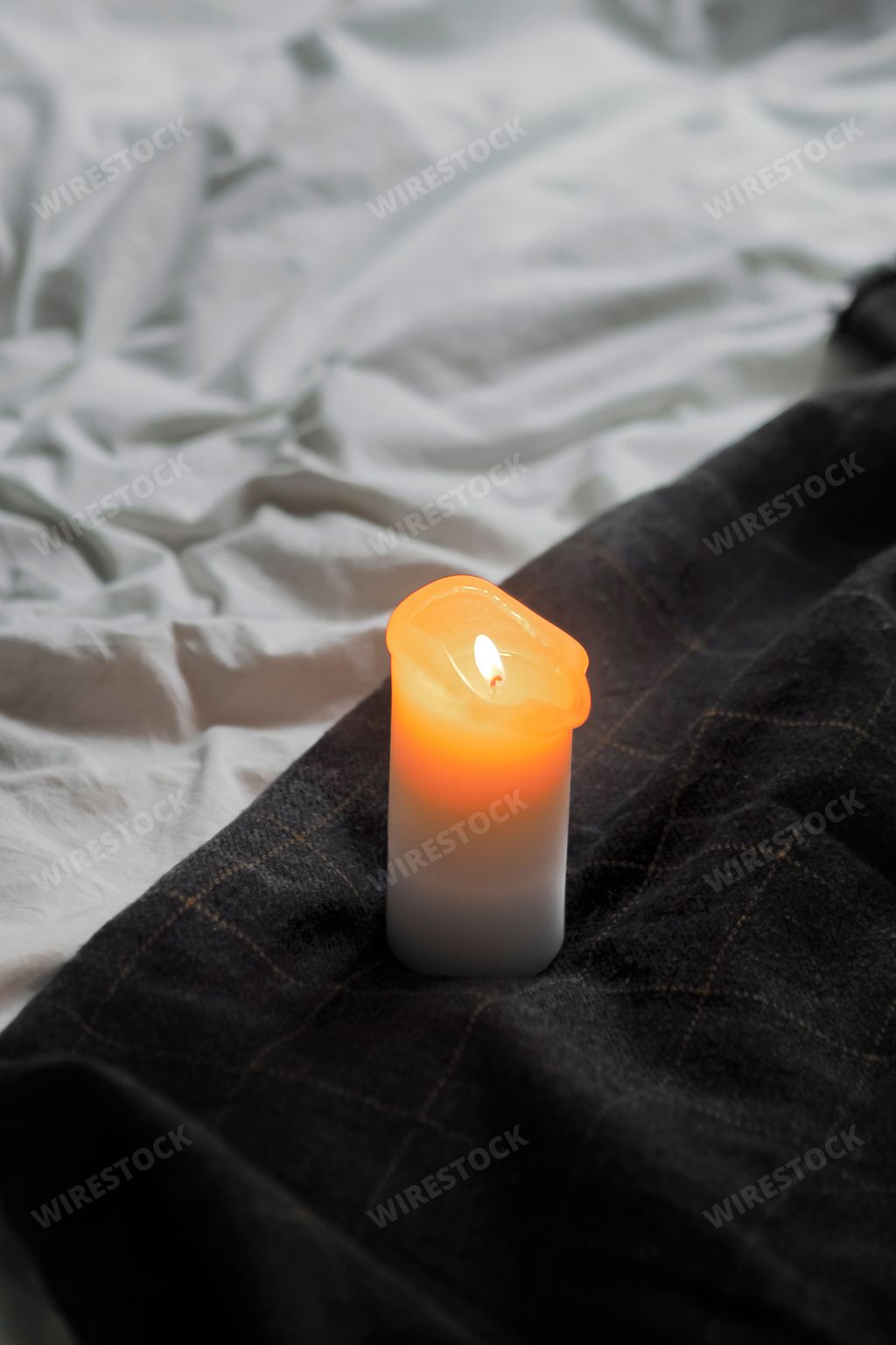 A white candle lit on a black linen-covered bed, creating a peaceful and serene atmosphere