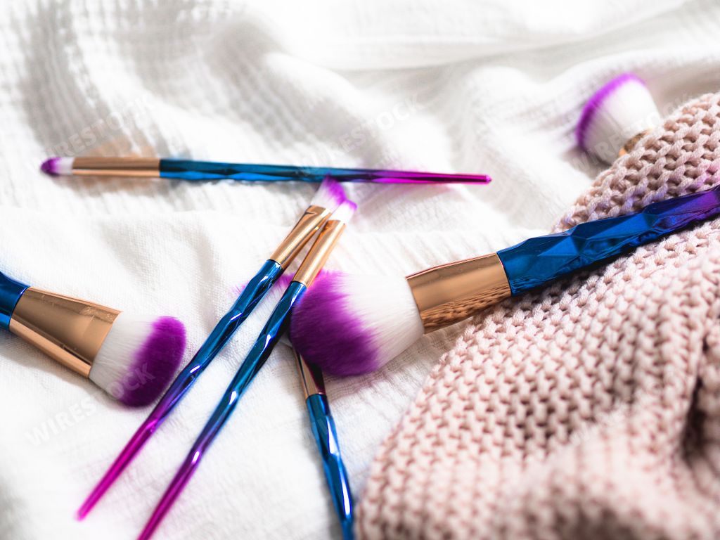 A closeup shot of numerous purple and blue makeup brushes on a white cloth