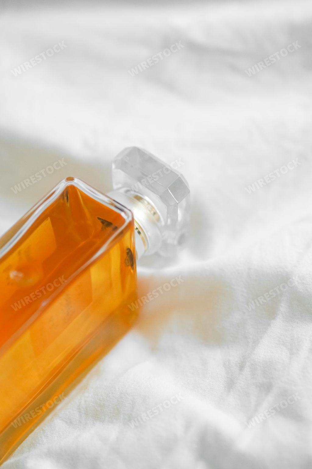 A vertical shot of a luxury perfume bottle on a white bedsheet