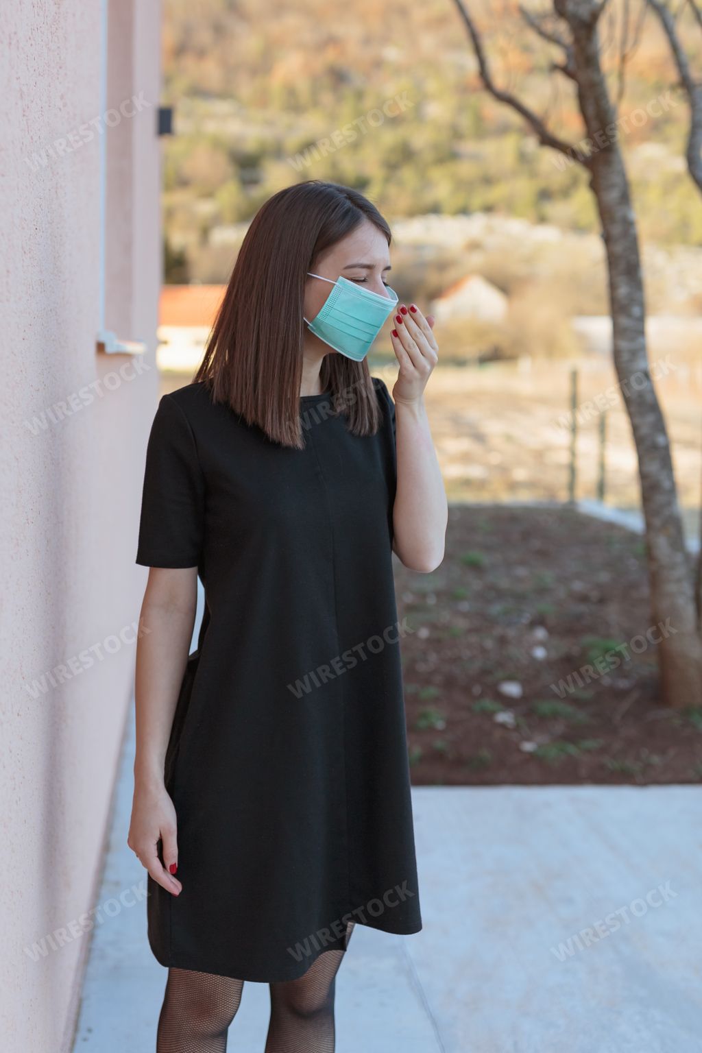 A vertical shot of a Caucasian female coughing while wearing a face mask during the covid-19 pandemic
