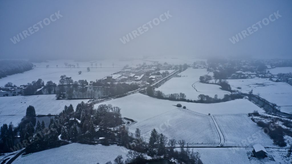 An aerial view of cultivated fields covered in snow on a foggy weather
