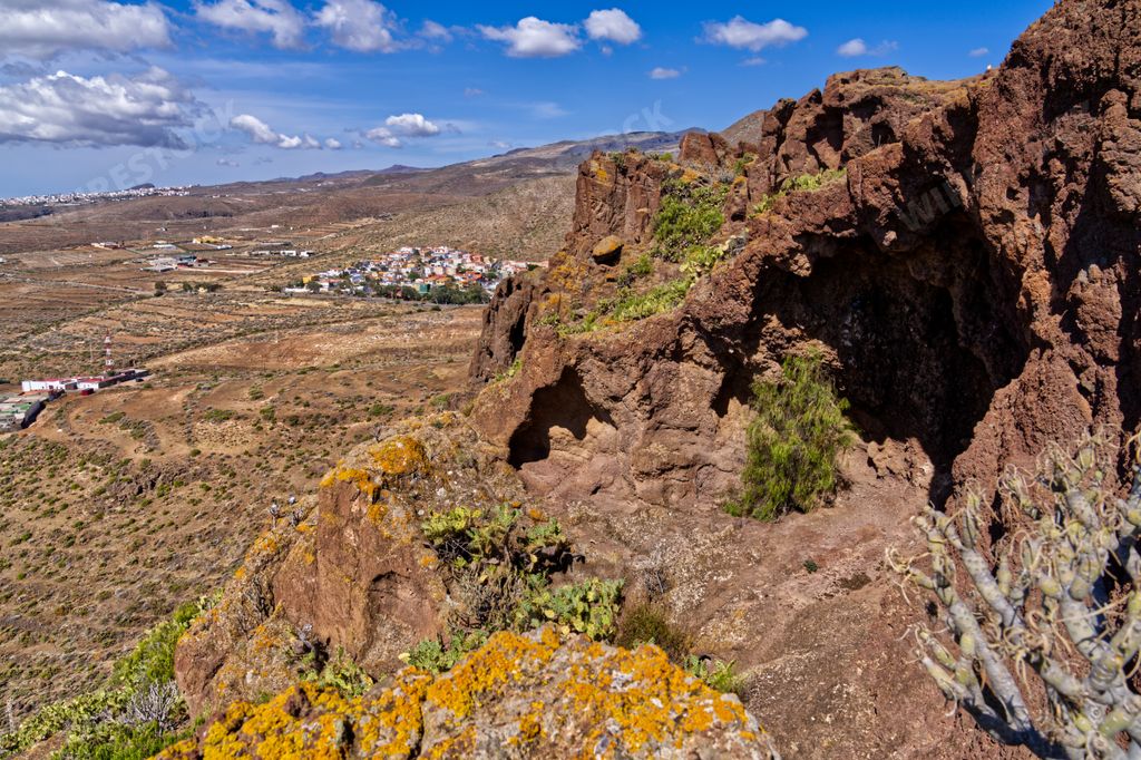 A scenic view of a village seen behind a rocky mountain on a sunny day